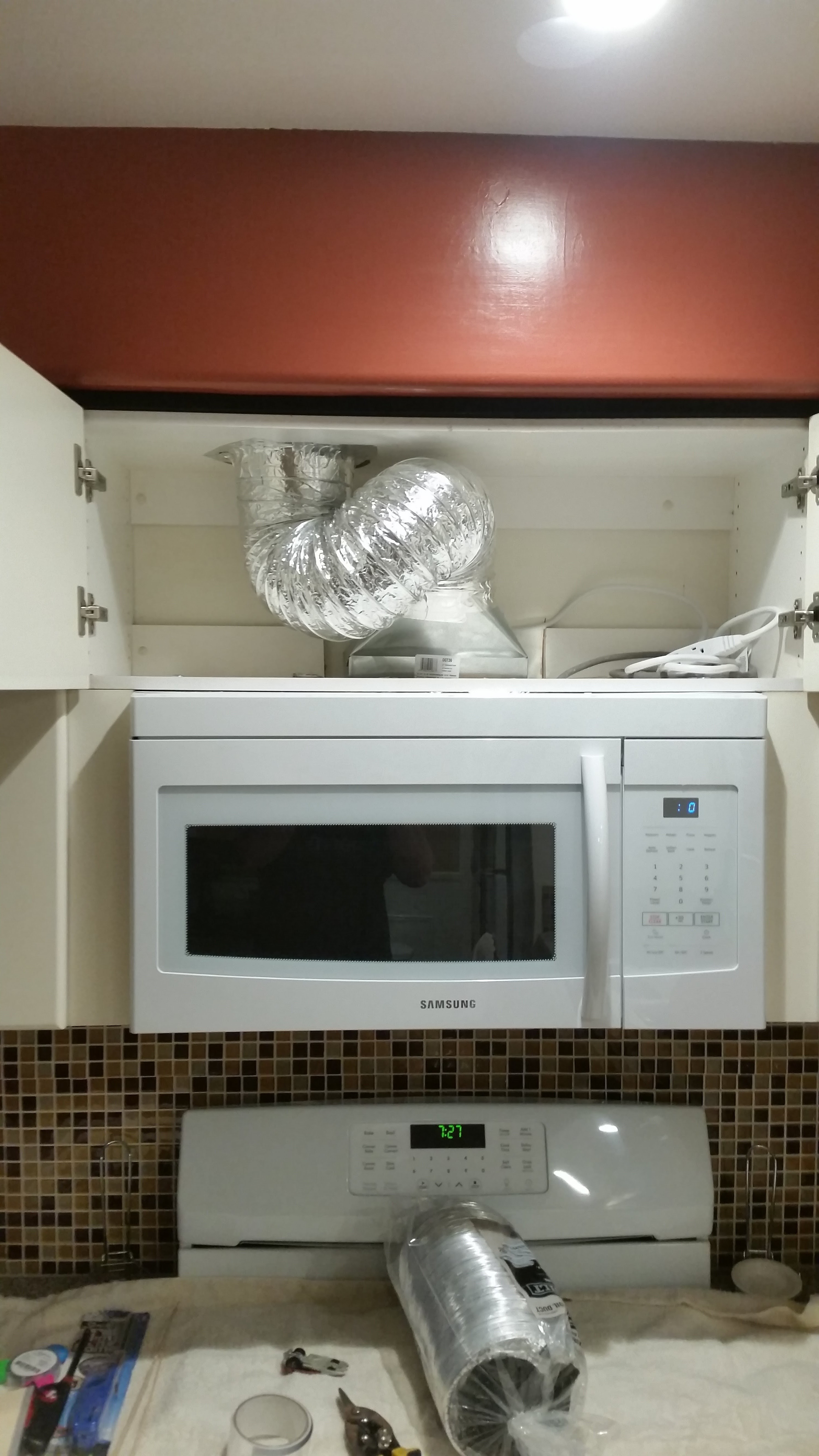 Two hands hold the drywall as someone is installing it over a drywall panel frame, cut out in the wall and white-drywalled...