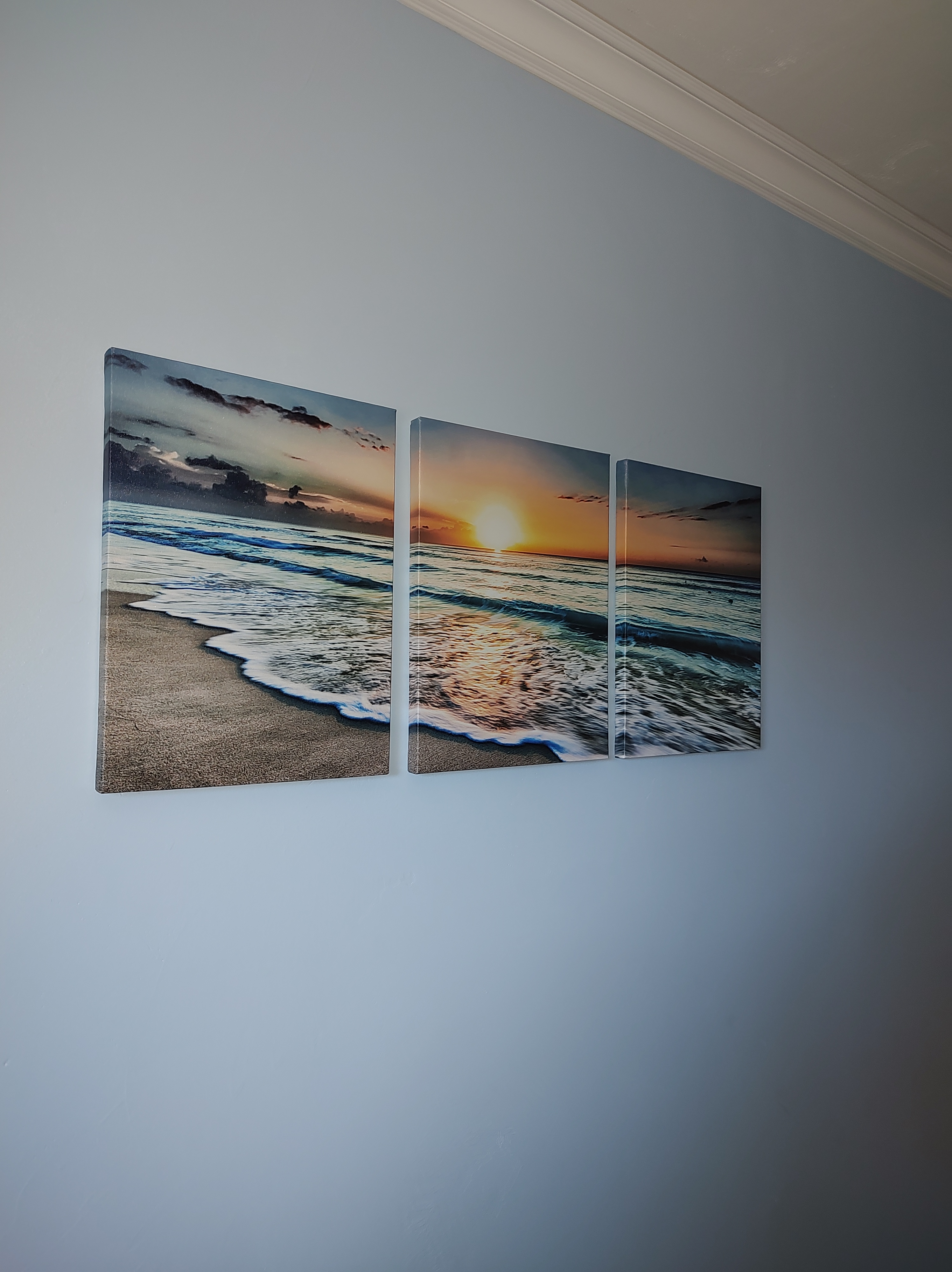 A man in a tan t-shirt and dark blue jeans is standing next to a white couch while holding a power drill by a wall-mounted...